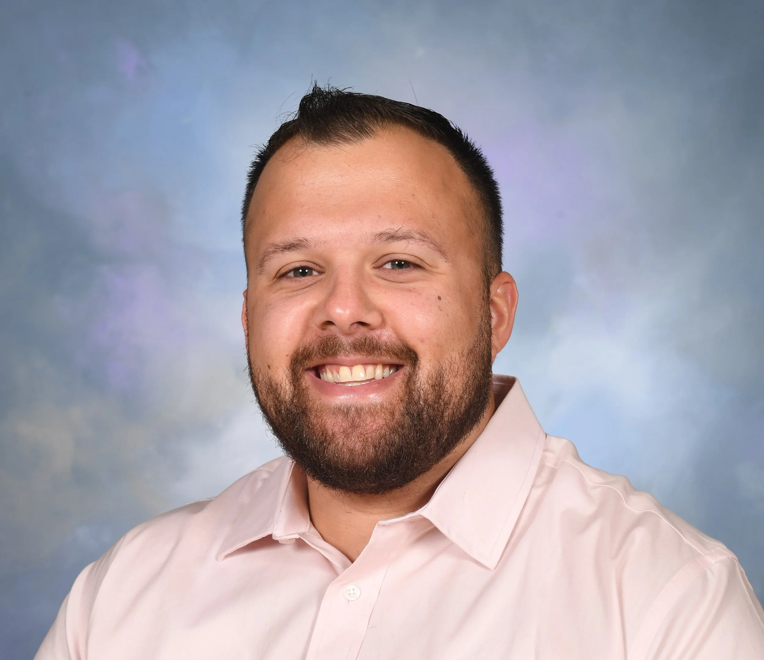 Kyle Deaver smiling in a light pink collared shirt against a blue and purple background